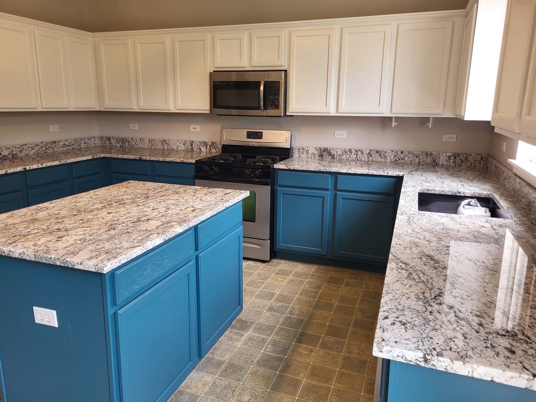 Kitchen with new granite countertops, centre island, white upper cabinets over teal bases, and a stainless gas range.