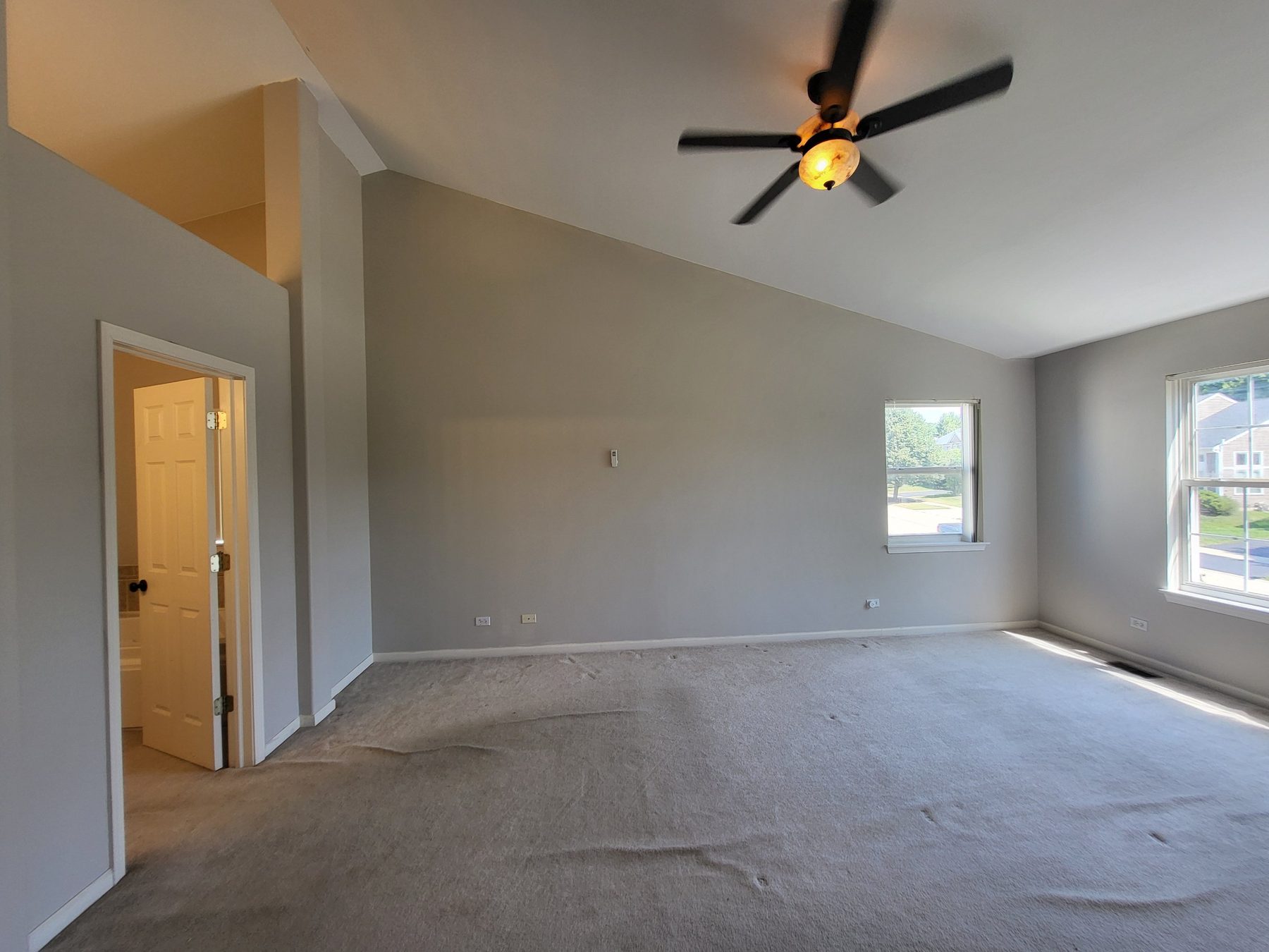 Primary bedroom with vaulted ceiling, ceiling fan and two front-facing windows, with the private bath beyond.